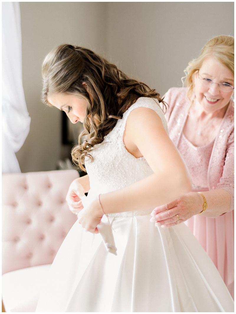 bride and mom putting on dress at wedding