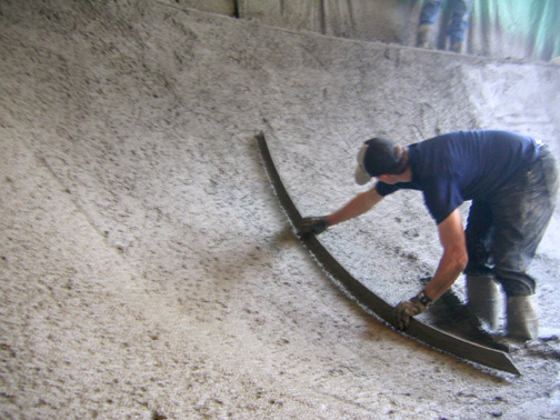 Worker hand-shaping concrete transition during skatepark construction