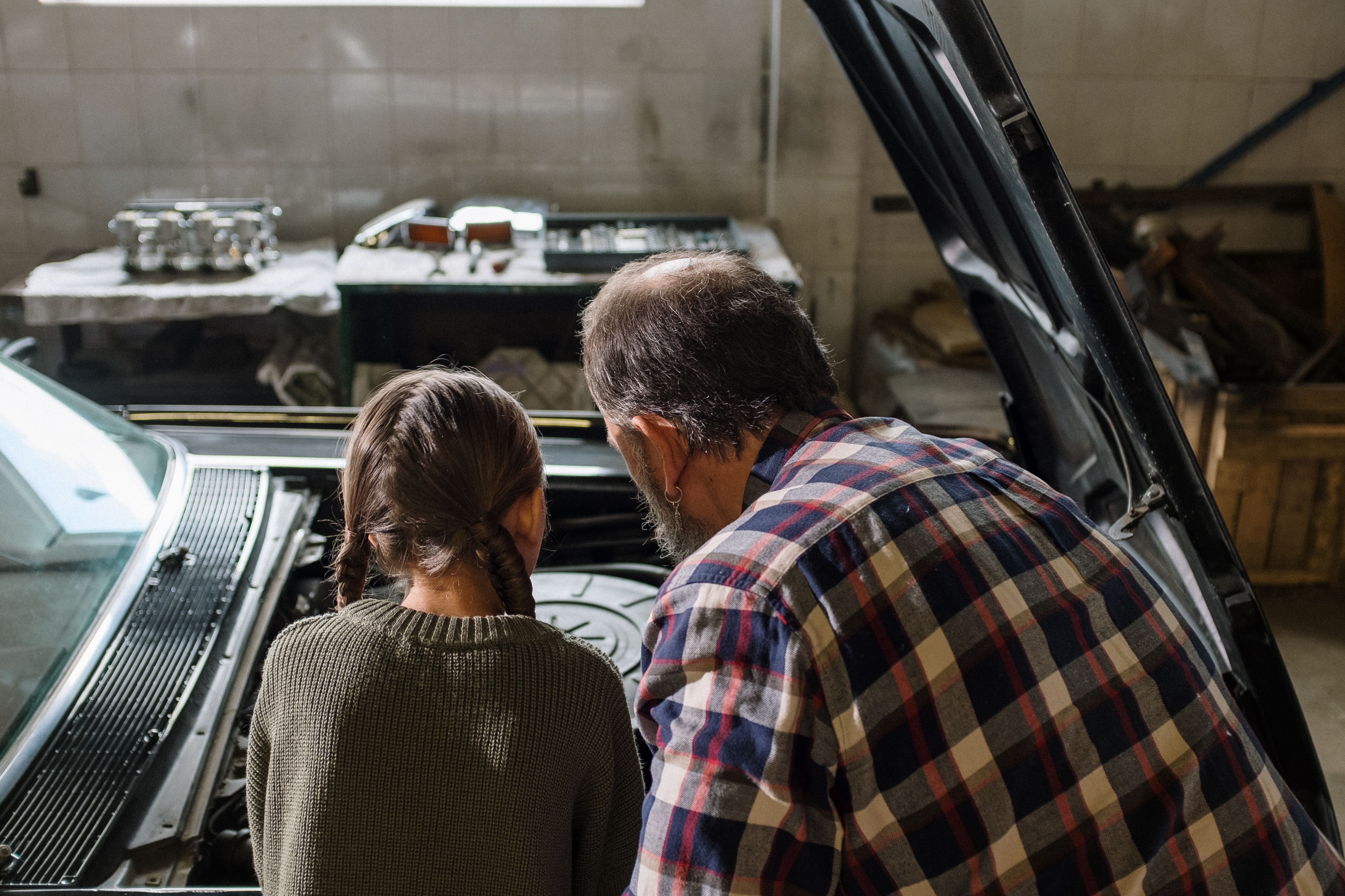 Older man teaching a young girl about a car engine