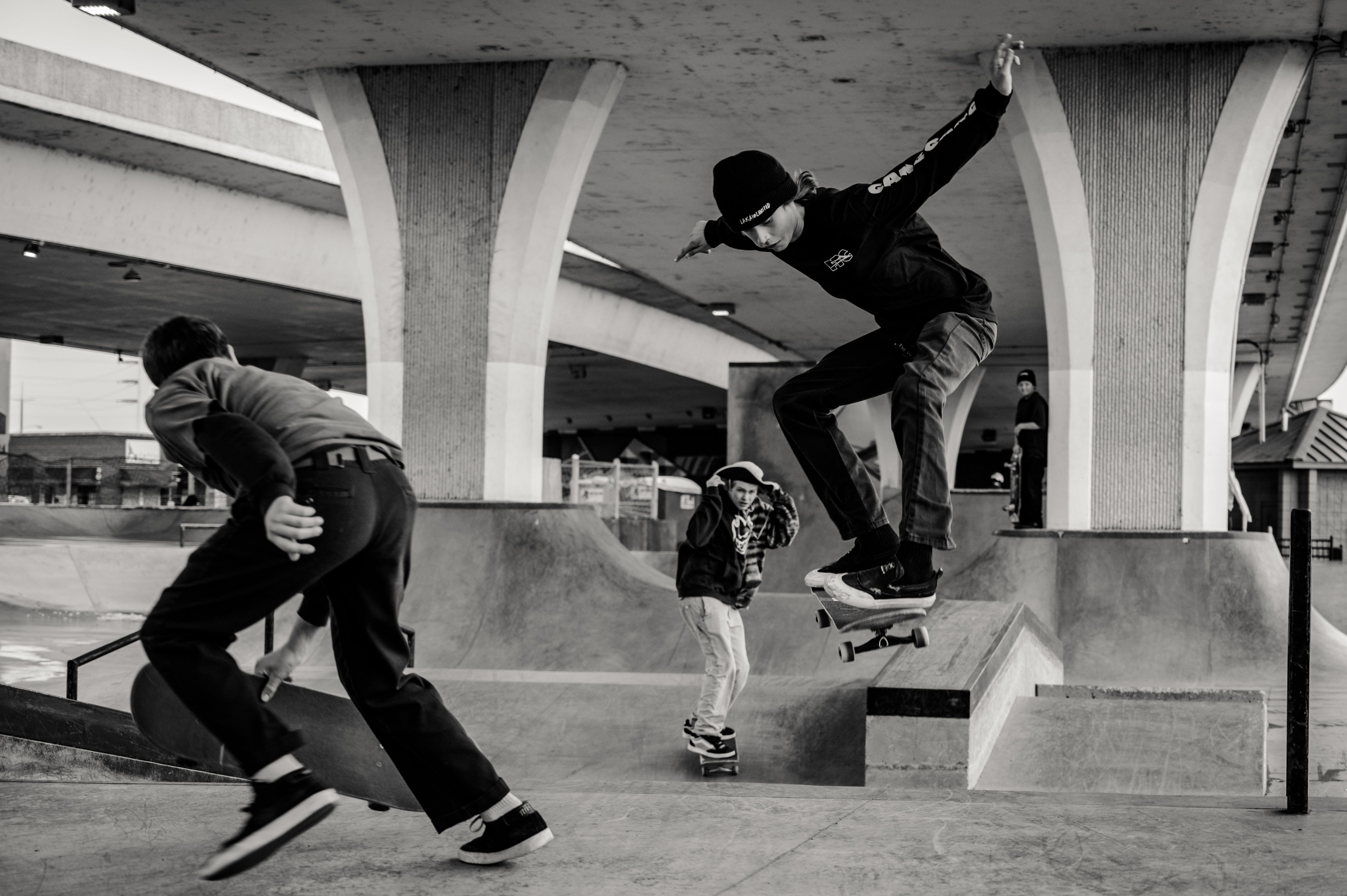Skaters moving through a concrete skate space beneath an overpass