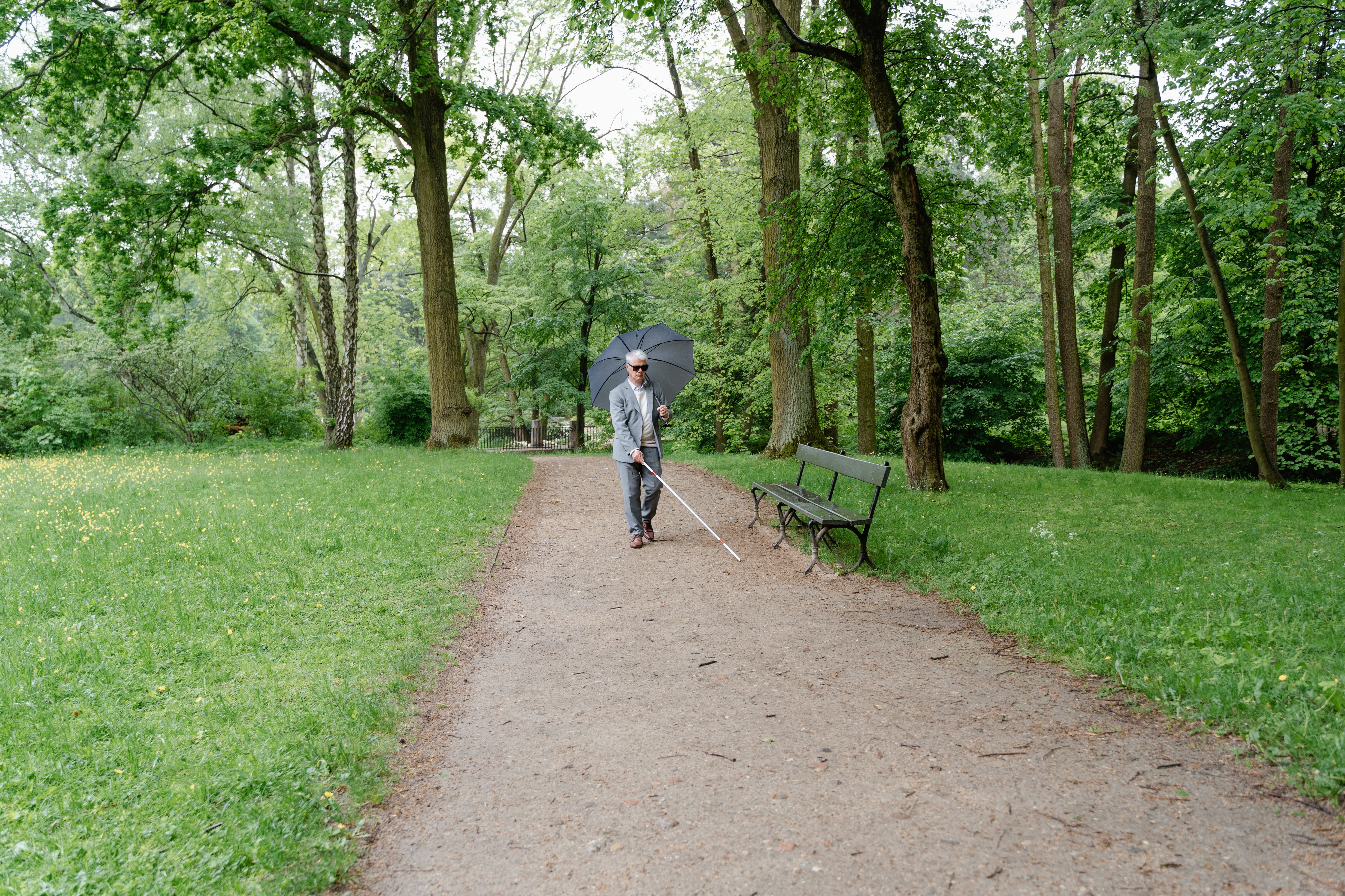 A blind pedestrian using a white cane independently on a broad park path