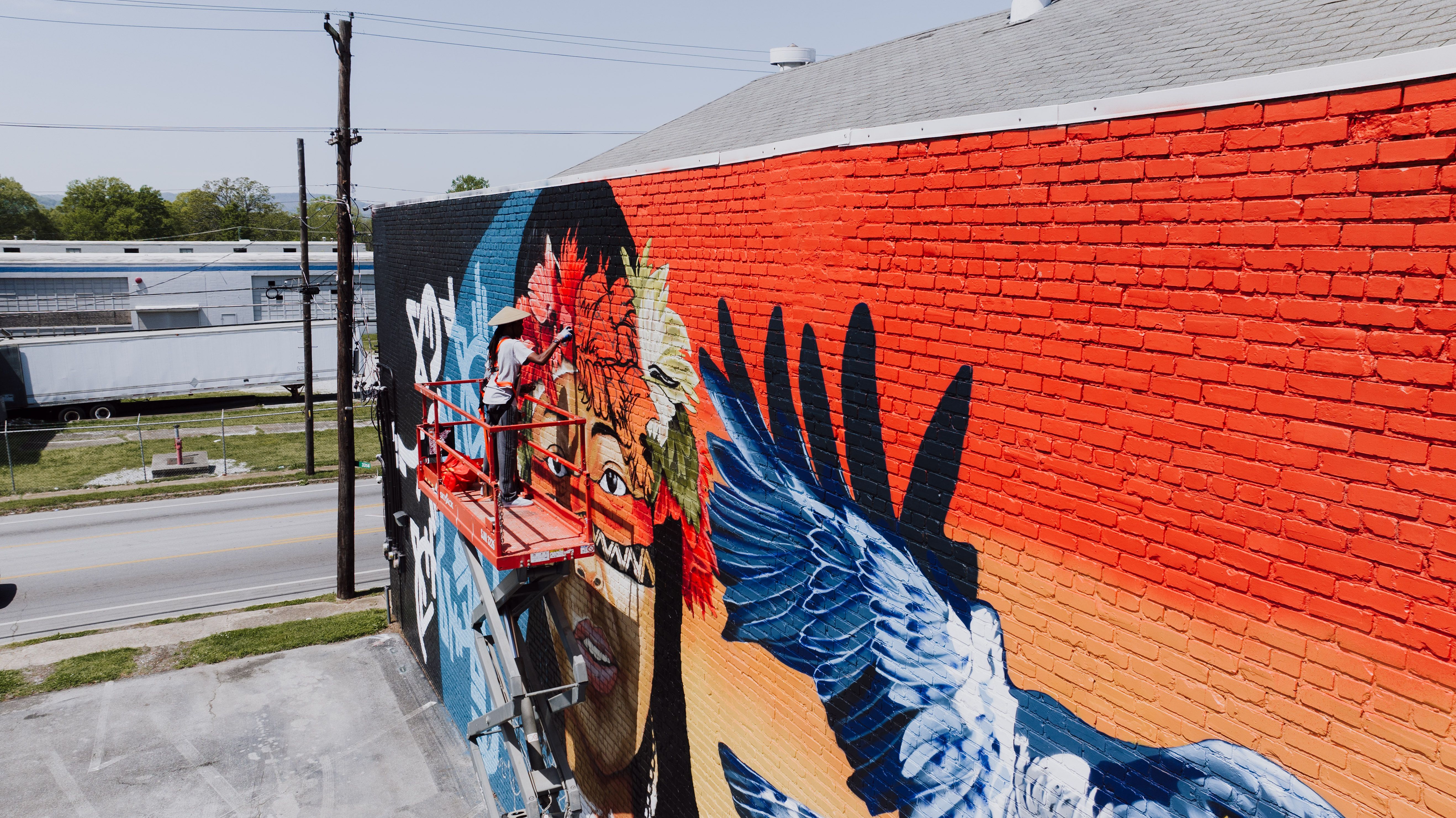 Artist painting a large public mural from an elevated work platform