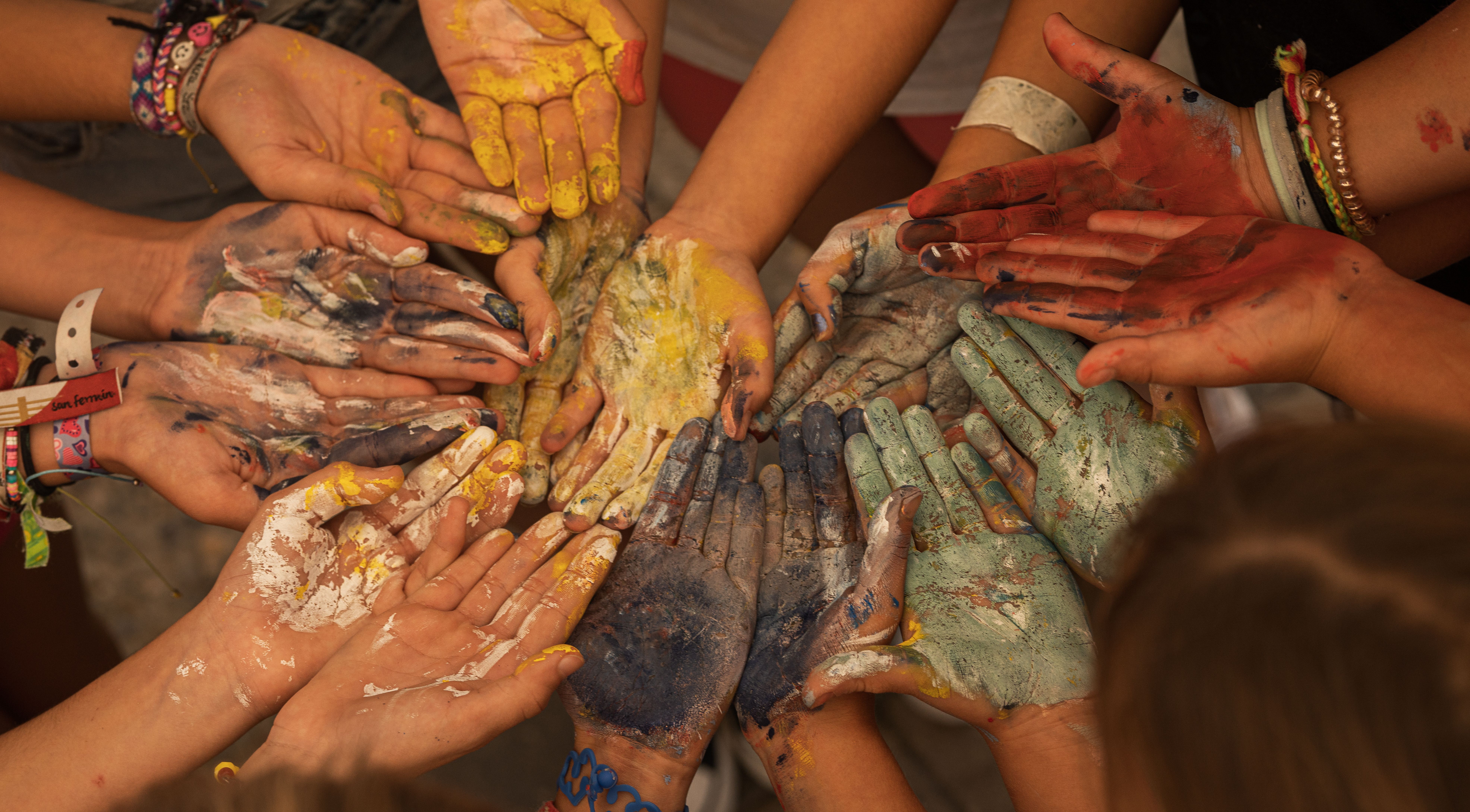 A circle of paint-covered hands reaching together in a collaborative art activity