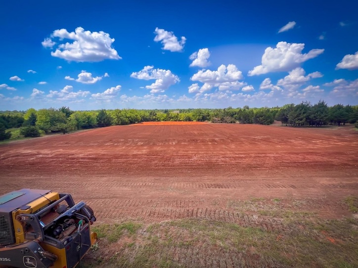 Finished graded building pad on red clay in Central Oklahoma with skid steer in foreground