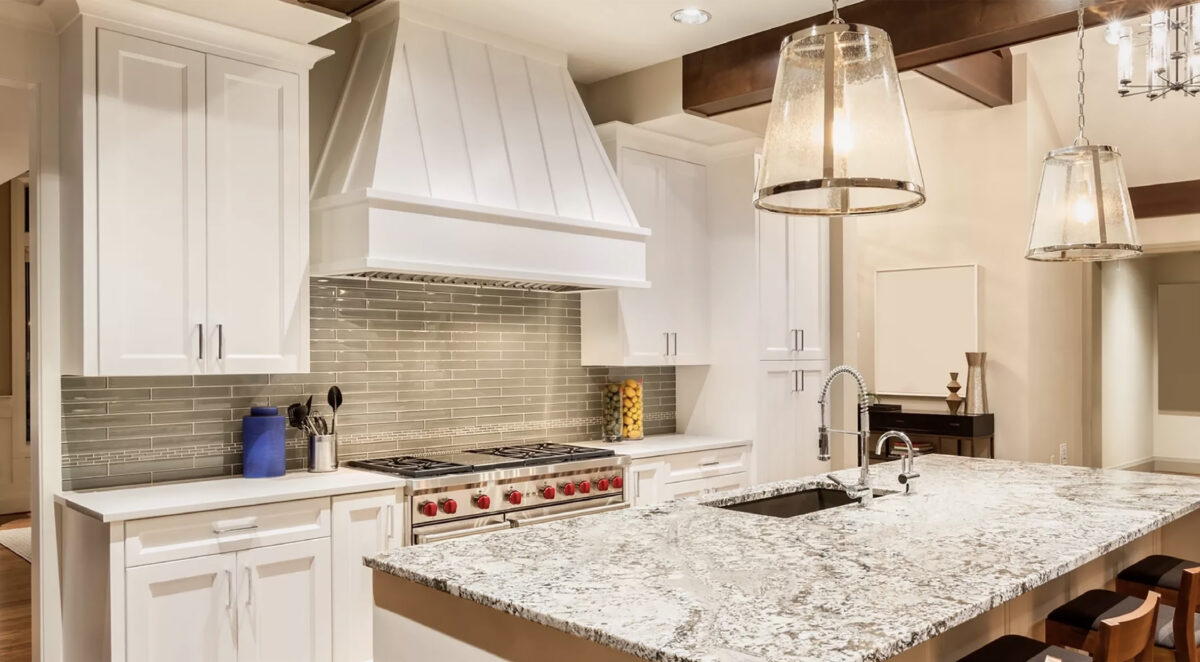 White kitchen with a custom paneled range hood, gas range and granite island