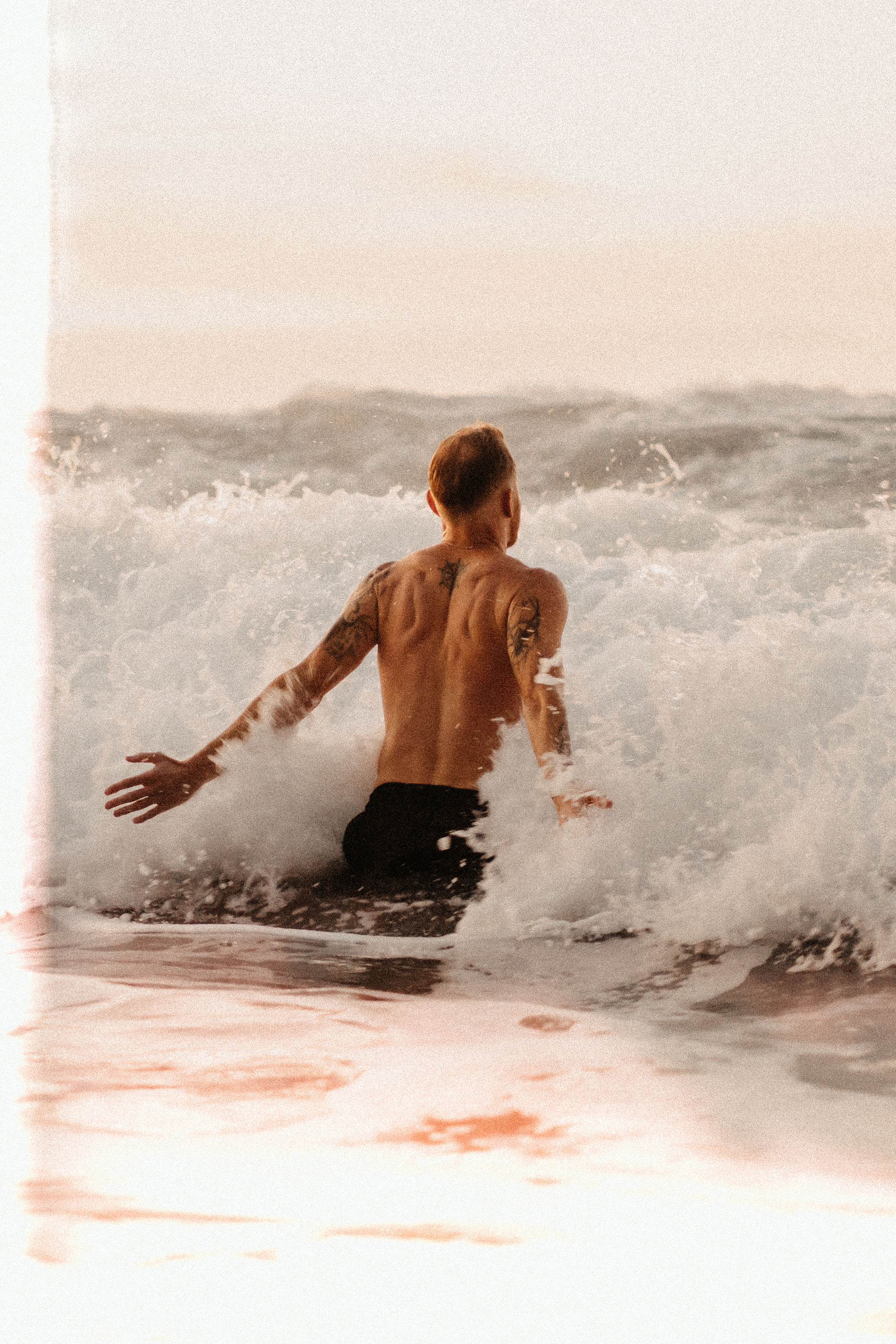 Patrick Thiele standing inside a breaking wave, arms open, seen from behind.