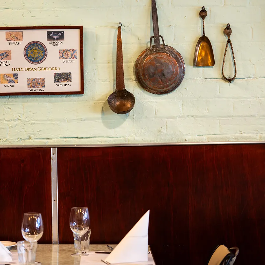 Vintage copper pans and framed Italian prints above a set table at Grappino