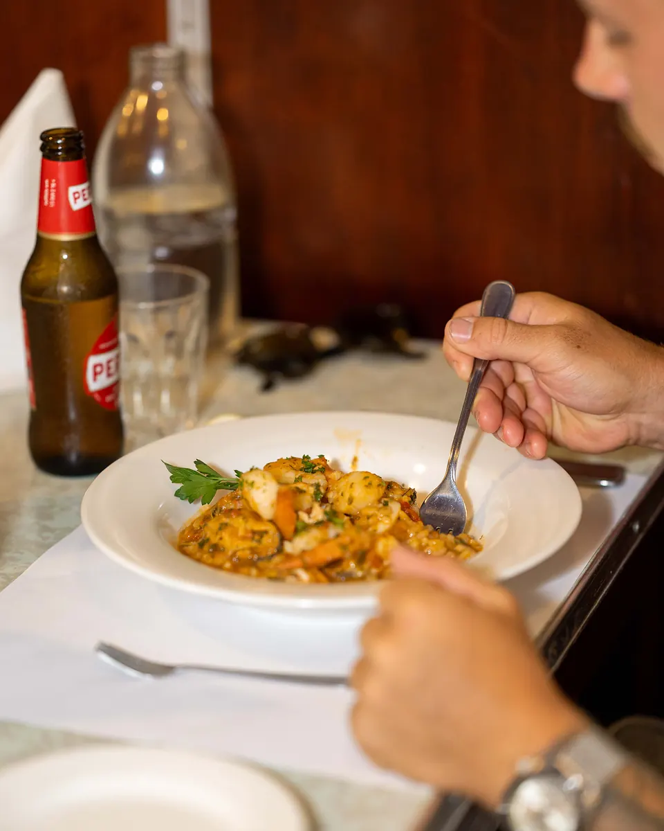 A cold beer beside a bowl of pasta at a Grappino table
