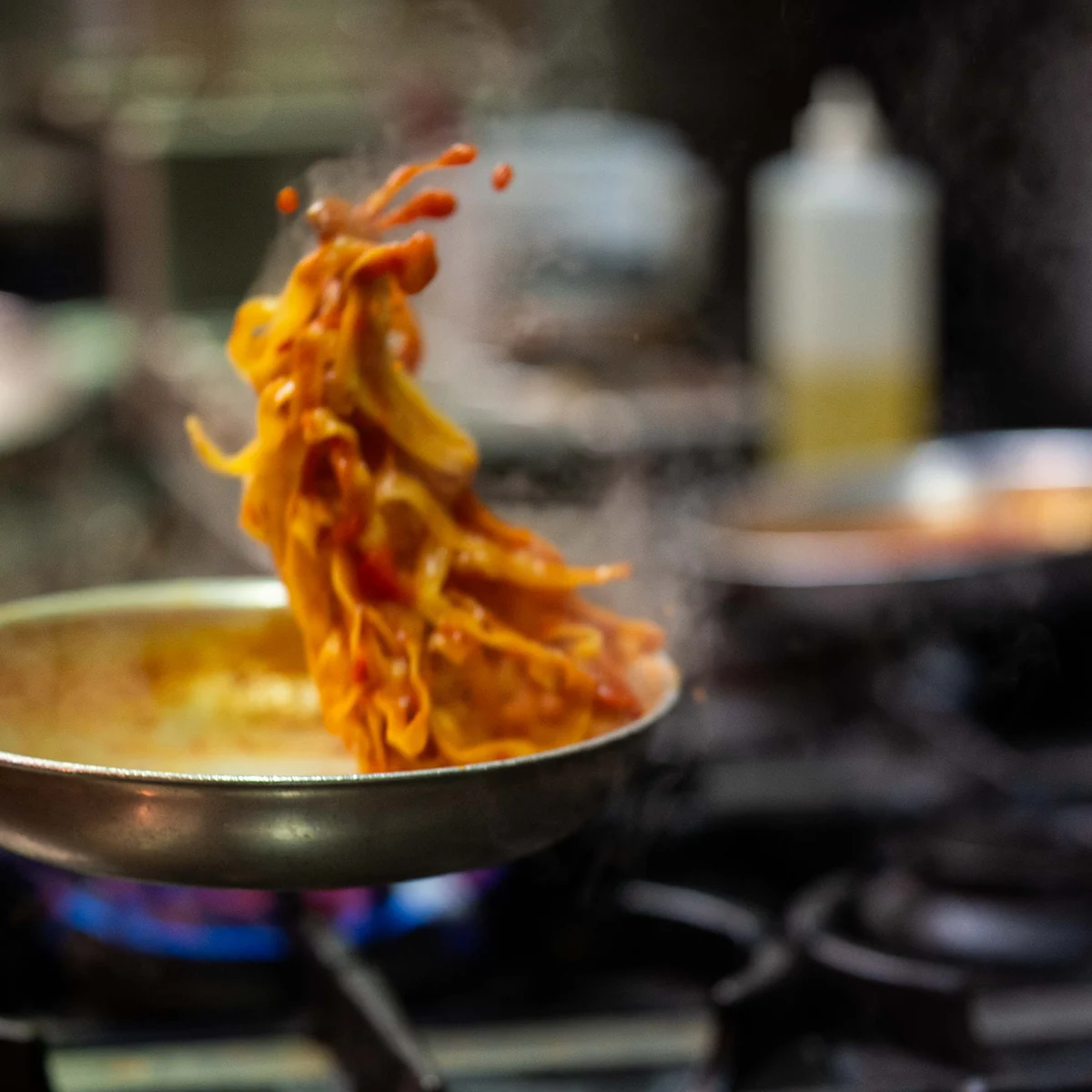 Pasta tossed high above a pan of tomato sugo on the burner at Grappino