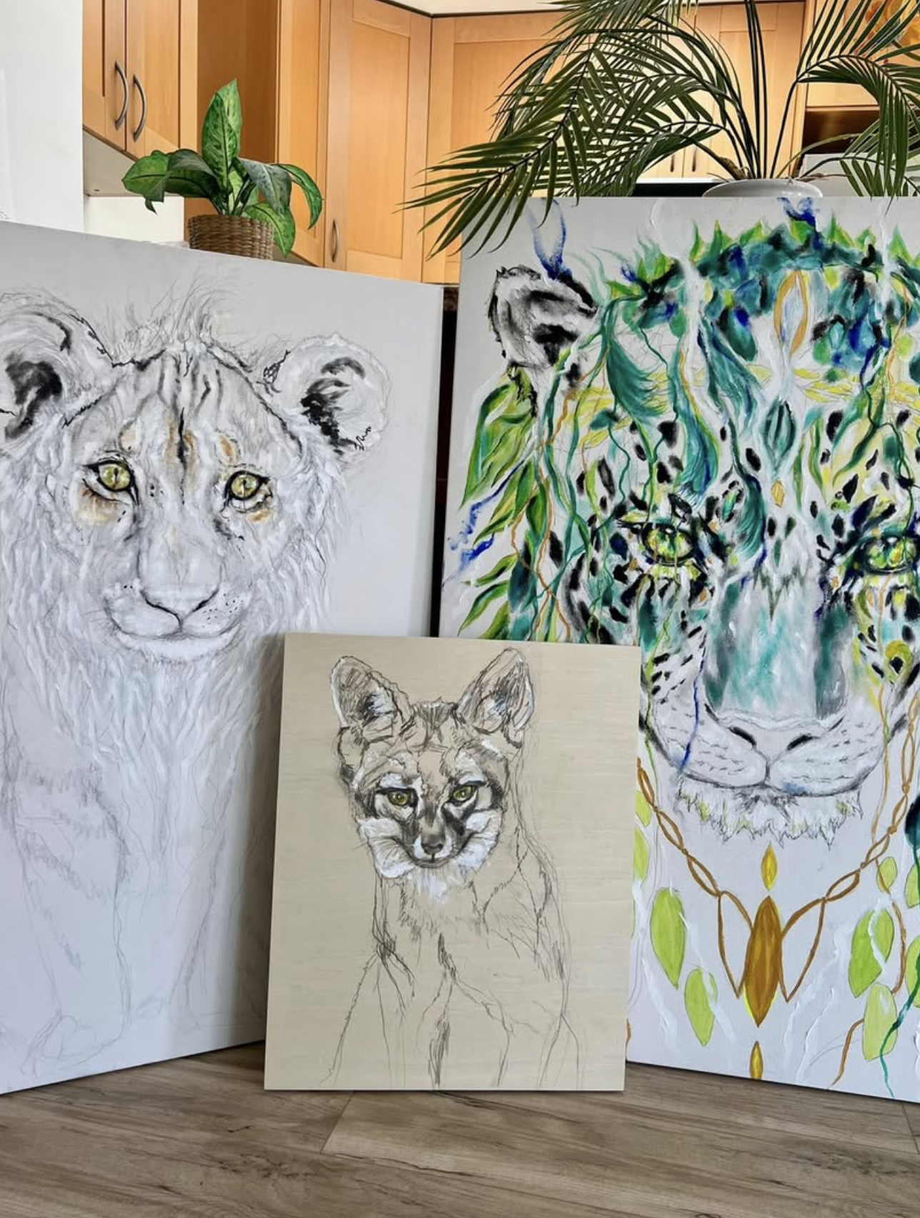 Three canvases in Paula's studio — a lioness, a cougar cub, and a green leopard
