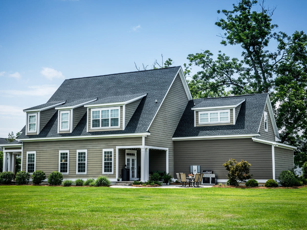 Large modern two-story house with gray siding, white trim, and a black shingled roof, surrounded by a well-manicured lawn.