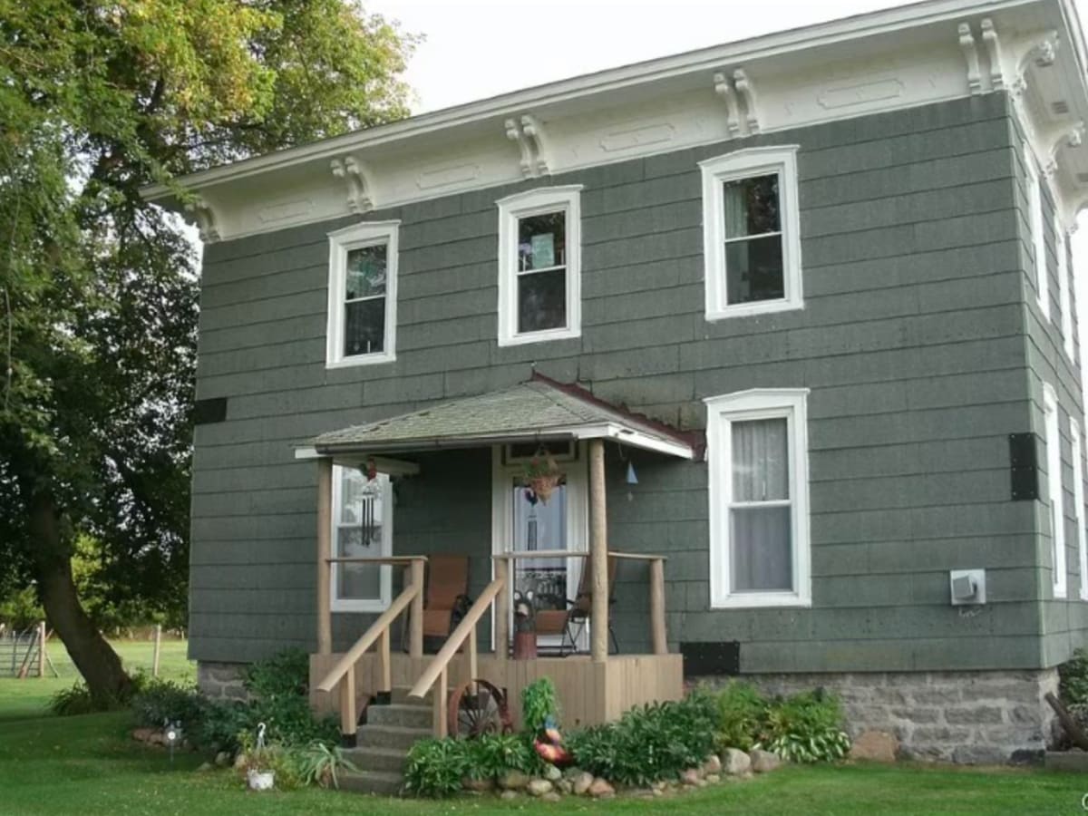 Historic two-story farmhouse with gray siding and a small porch with wooden steps.