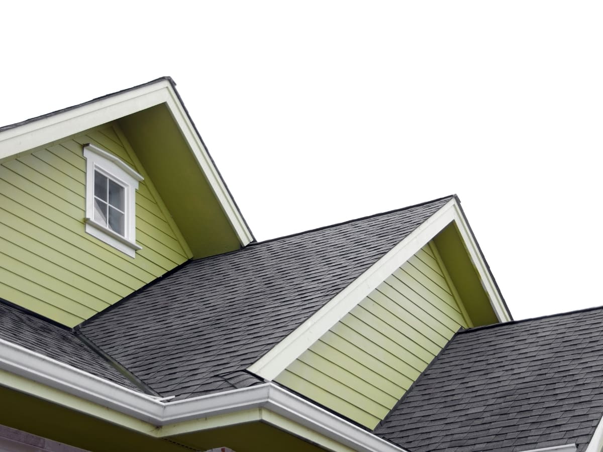 Close-up of a house’s roof and gable with green siding and asphalt shingles, showcasing the contrast between the light green walls and dark roof.