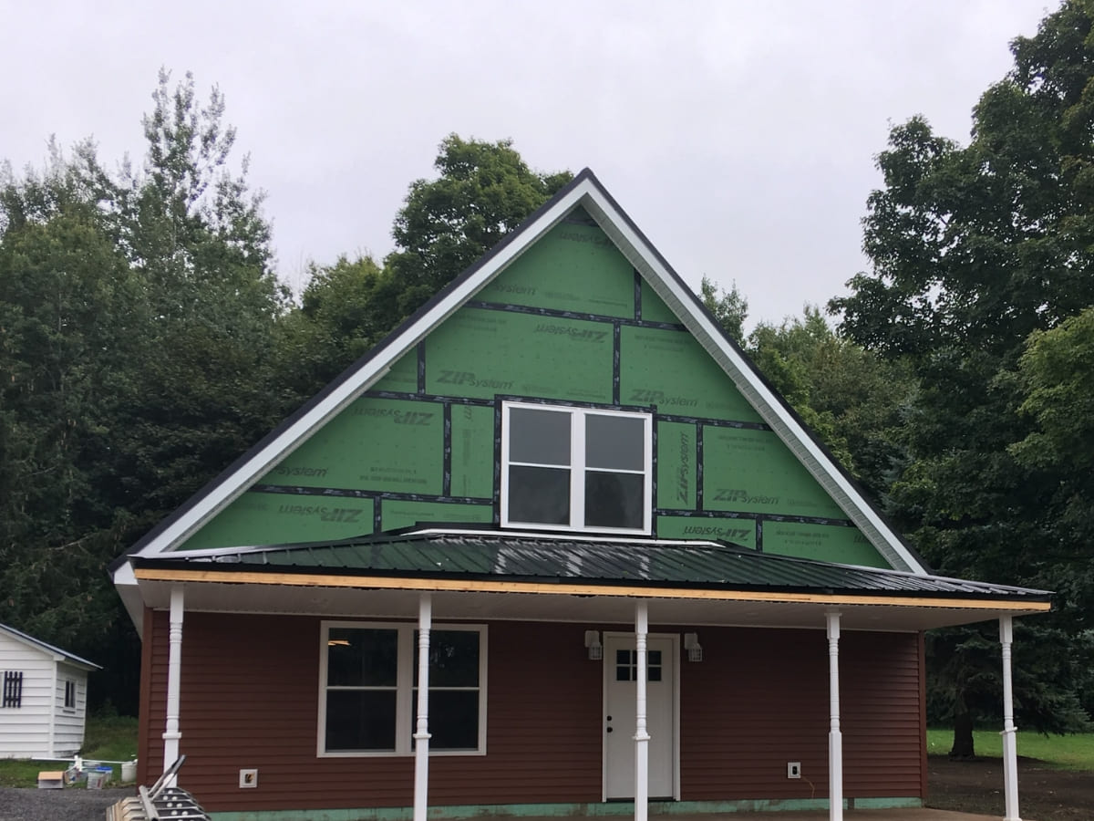 House under construction with green exterior sheathing and a metal roof.