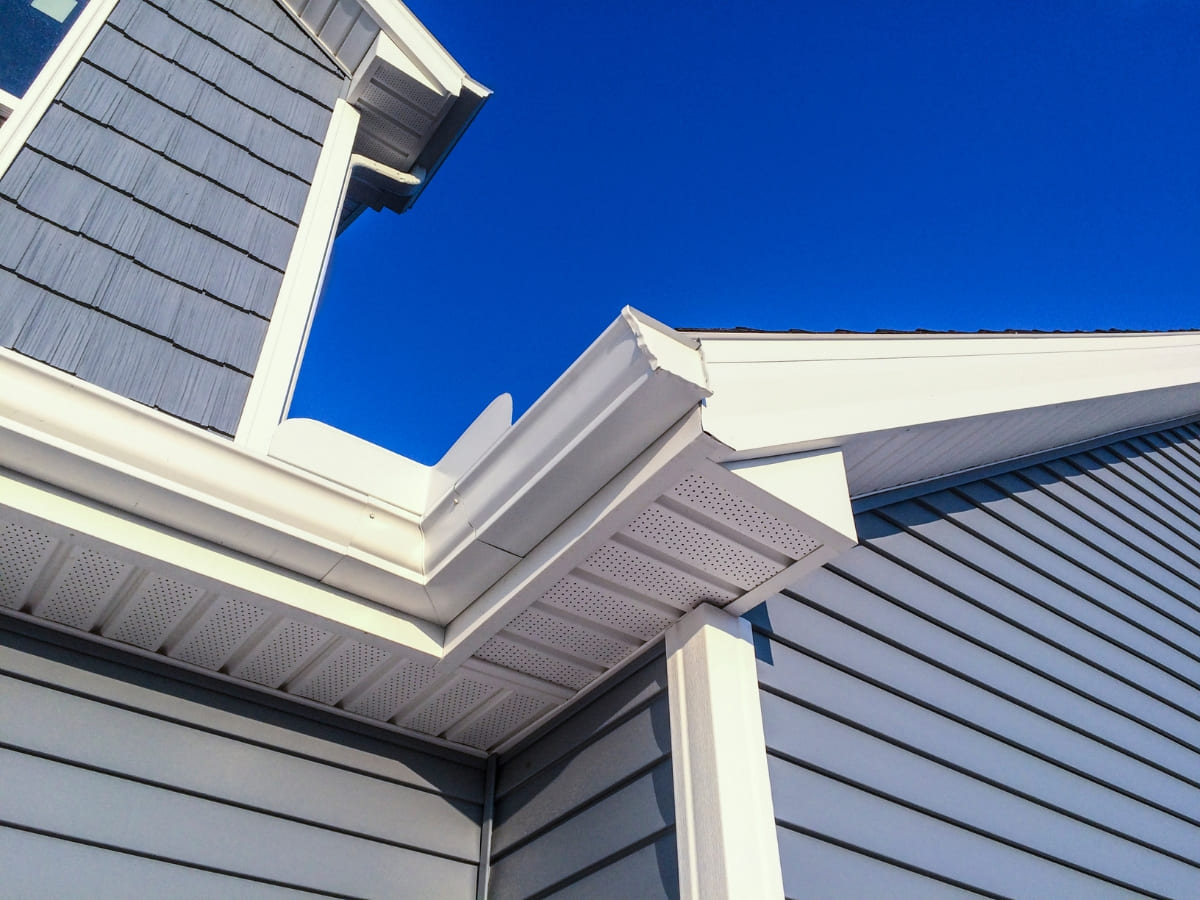 Partial view of a house’s roofing, gutters, and siding, highlighting the intersection of the roof and the house’s exterior.