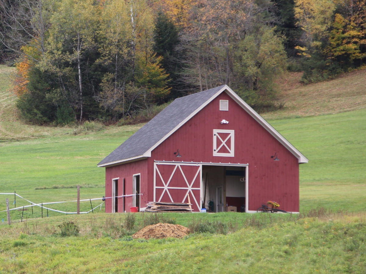 Red barn with white trim set against a backdrop of green fields and autumn trees