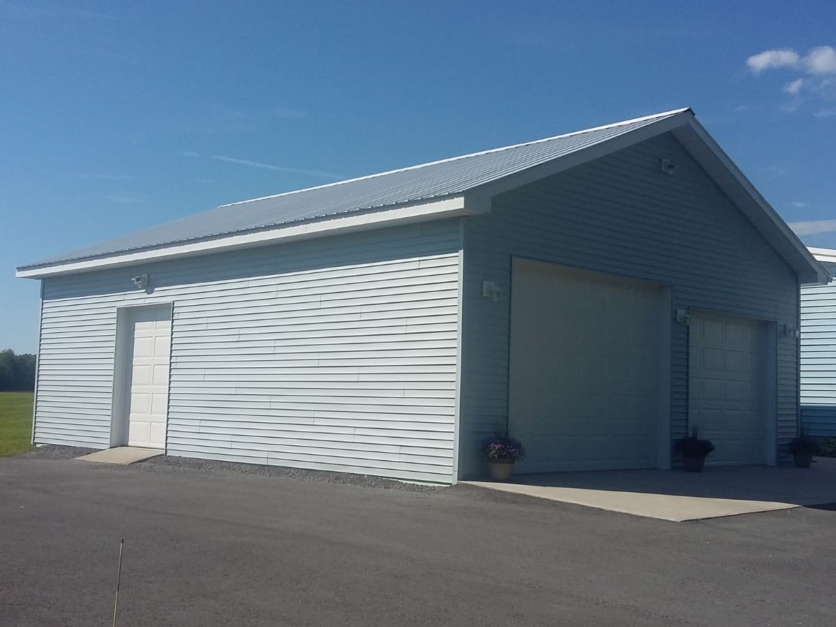 Detached light blue garage with a metal roof and white garage doors, set on a paved driveway.