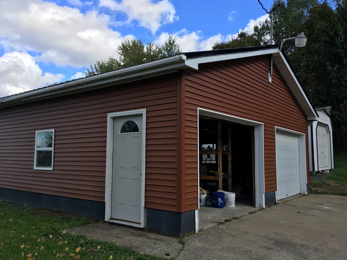 Detached garage with red siding, white doors, and a concrete driveway.