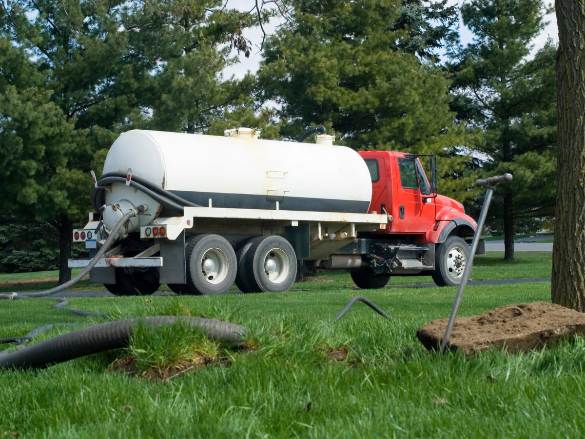 Septic pumping truck with a large white tank on a residential property, preparing for septic system maintenance.