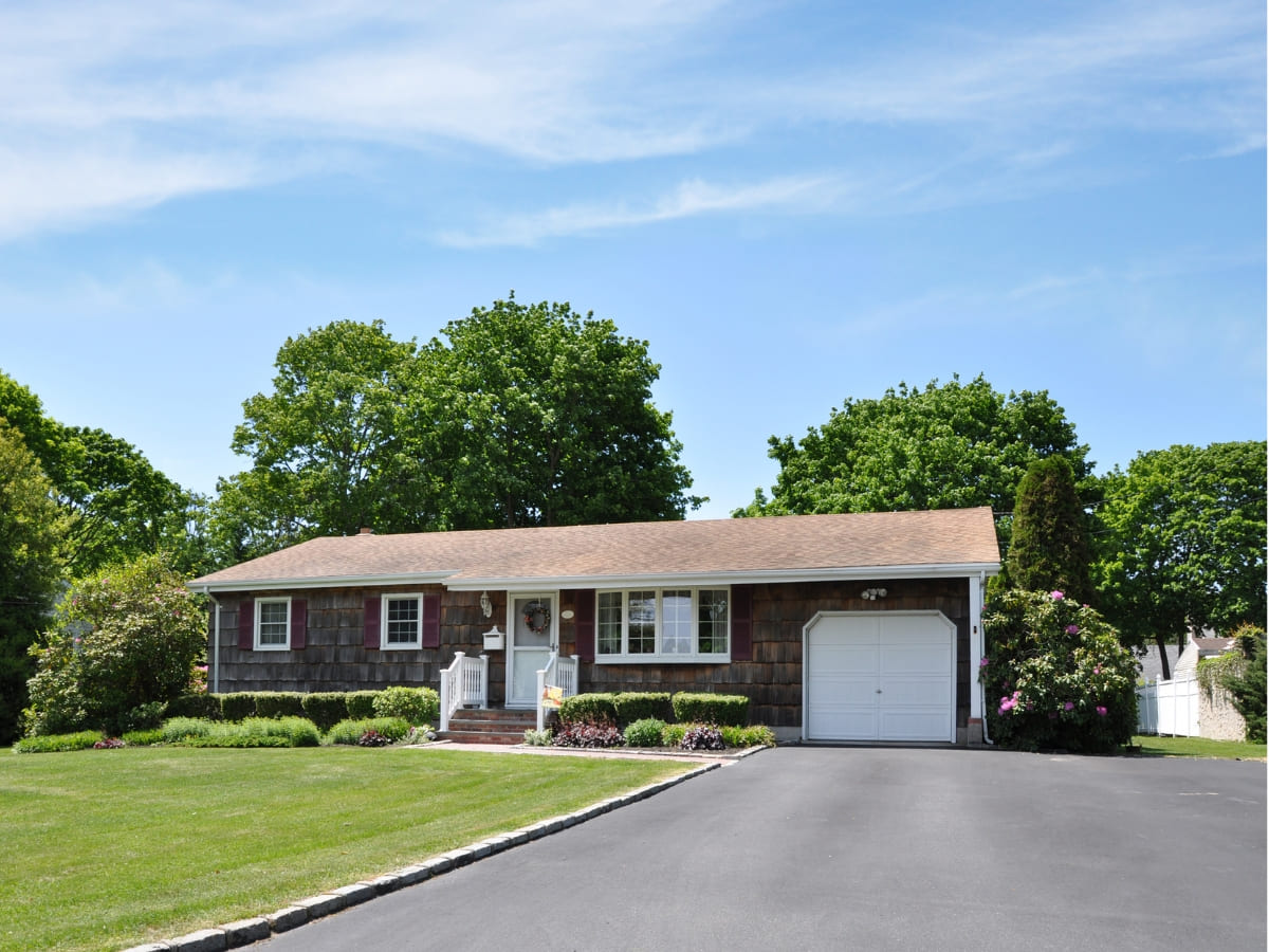 Single-story home with a paved driveway, well-maintained lawn, and neatly trimmed bushes, under a clear blue sky