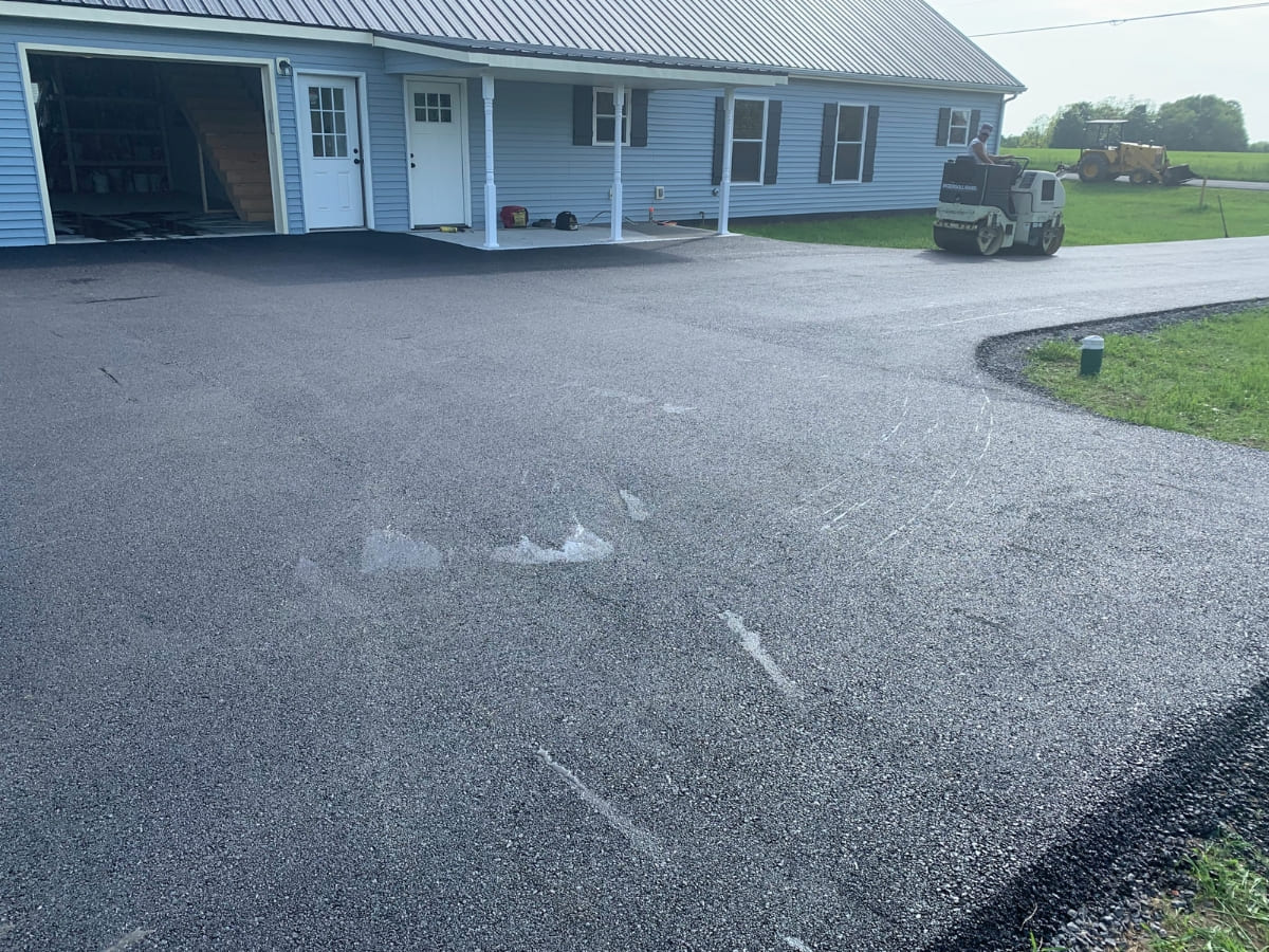 Close-up view of a newly paved driveway in front of a blue house with a white front door and garage doors