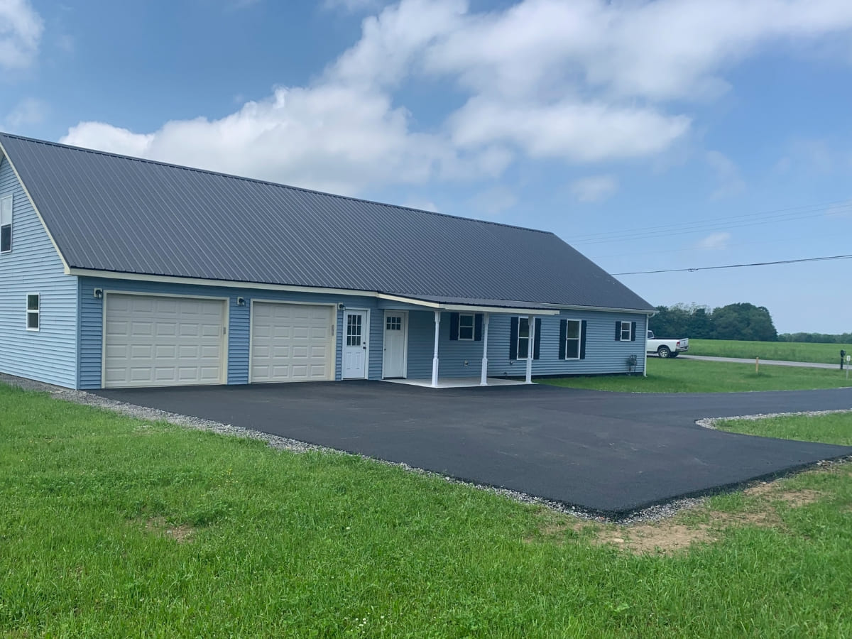 Newly constructed light blue house with a black metal roof, three garages, and an asphalt driveway.