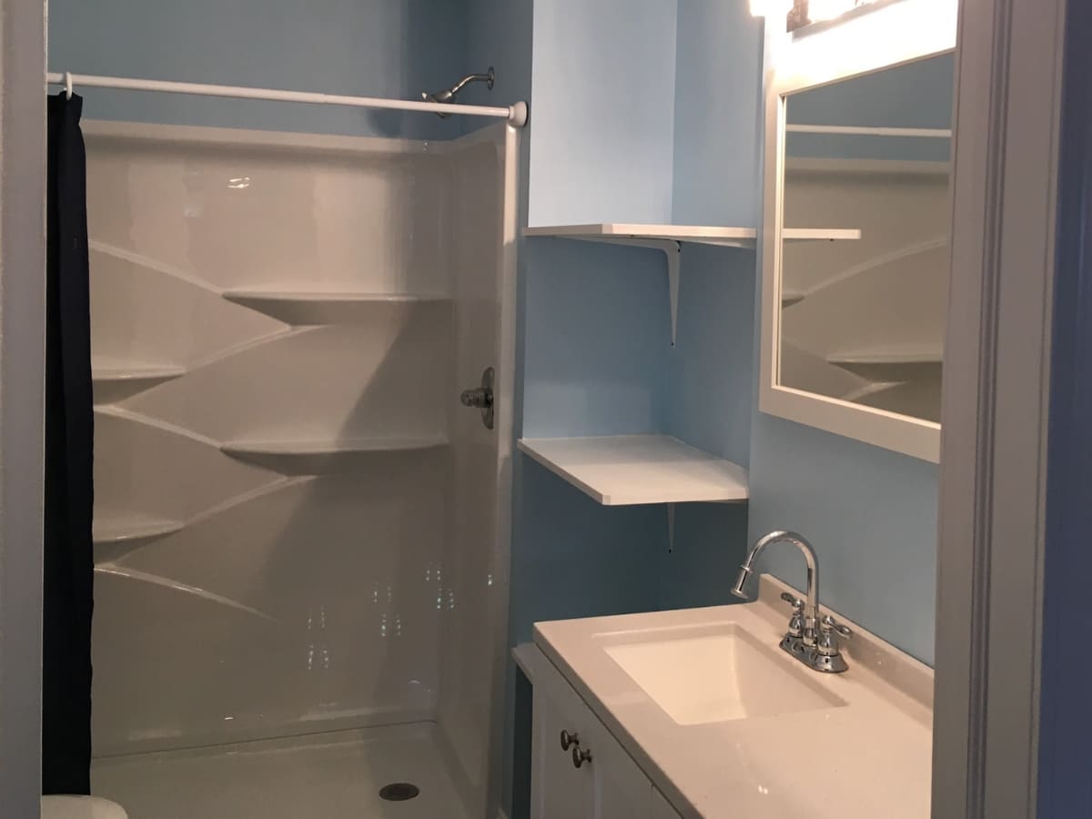 Compact bathroom with a walk-in shower, white vanity, and light blue walls.