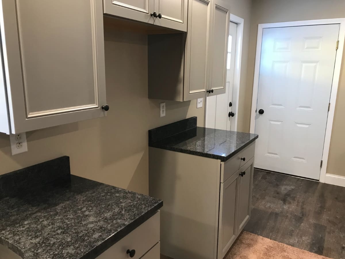 Modern kitchen with gray cabinets, granite countertops, and a white door