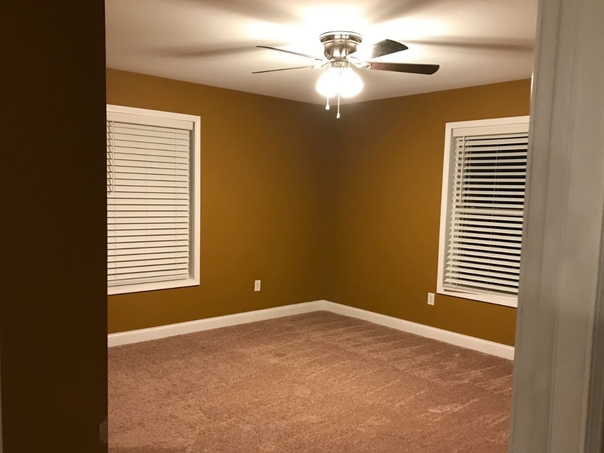 Bedroom with mustard-colored walls, white blinds, and a ceiling fan.