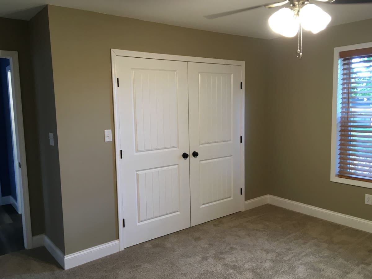 Bedroom with beige walls, white closet doors, and a ceiling fan.