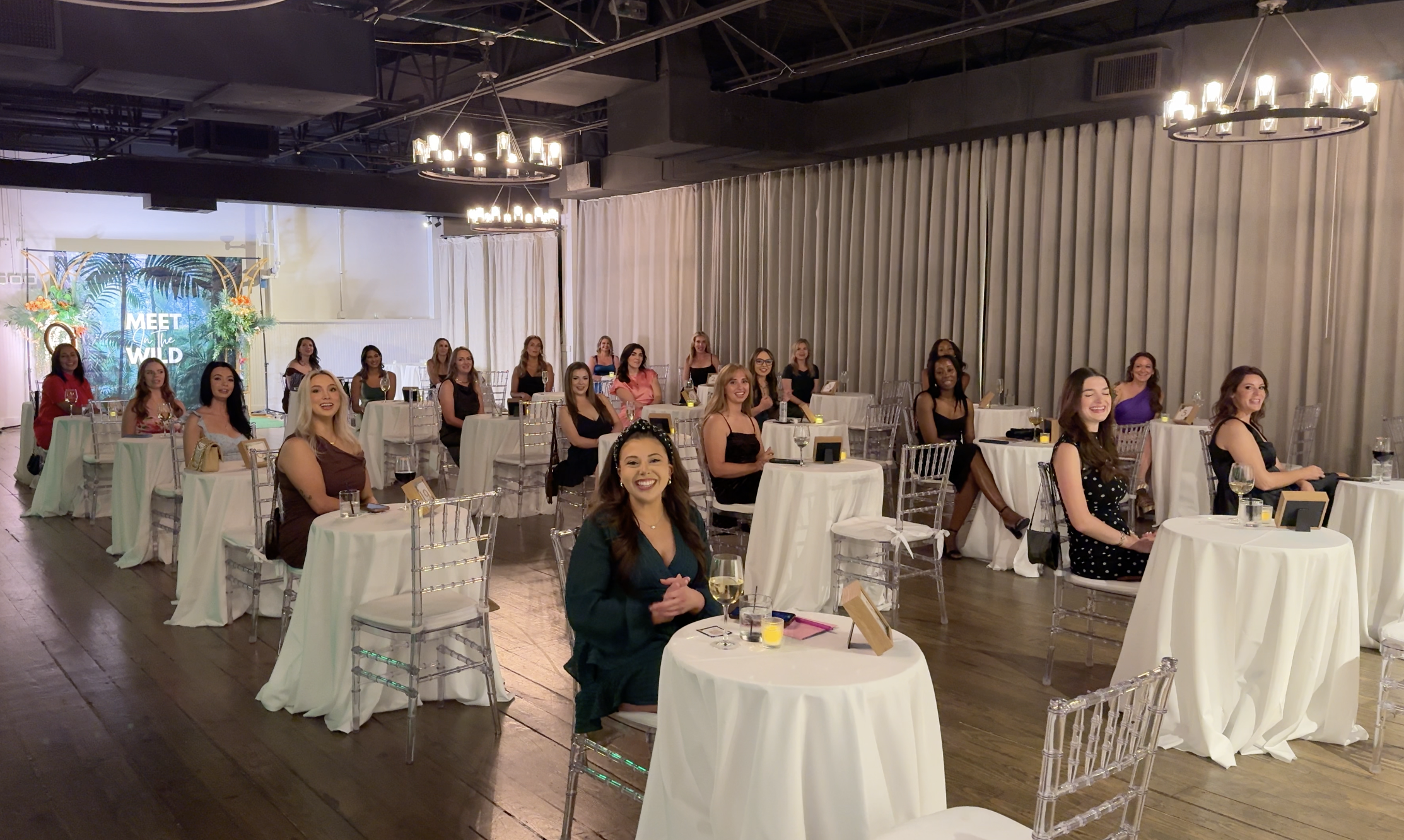 Packed room at a Meet In The Wild Dallas event — women at tables with MITW backdrop