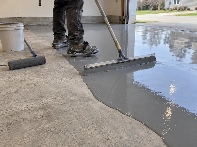 Spreading a gray epoxy base coat across a concrete garage floor with a squeegee