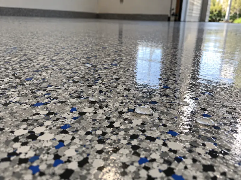Close-up of a full-broadcast epoxy flake floor with water beading on the glossy polyaspartic topcoat