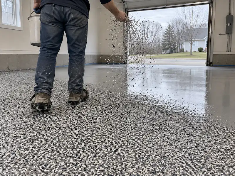 Installer in spiked shoes broadcasting decorative flake into a wet epoxy base coat