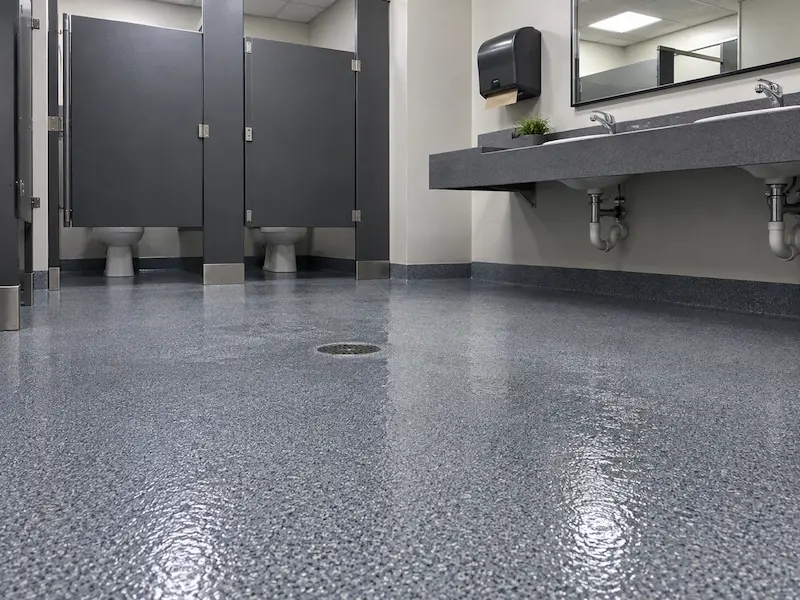 Commercial restroom with partition stalls and a seamless coated floor with no grout lines