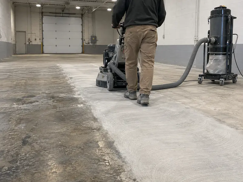 Walk-behind diamond grinder connected to a dust extractor grinding a commercial concrete floor