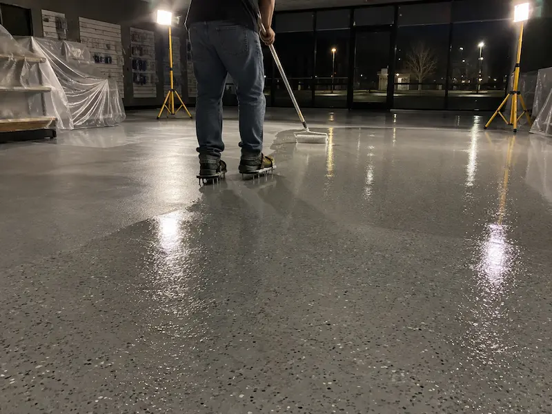 After-hours floor coating in a closed retail store, lit by portable work lights, with shelving covered in plastic