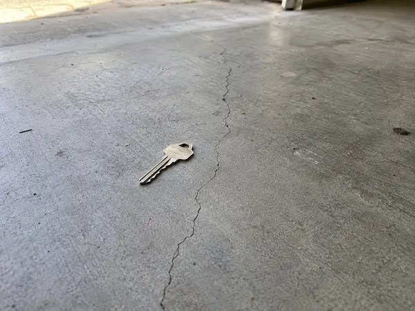 Thin hairline crack wandering across a concrete garage floor, with a house key beside it for scale
