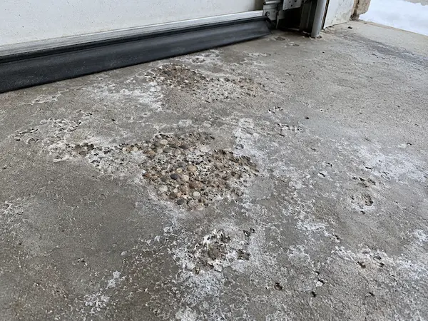 Spalled and pitted concrete with white road-salt residue just inside a garage door