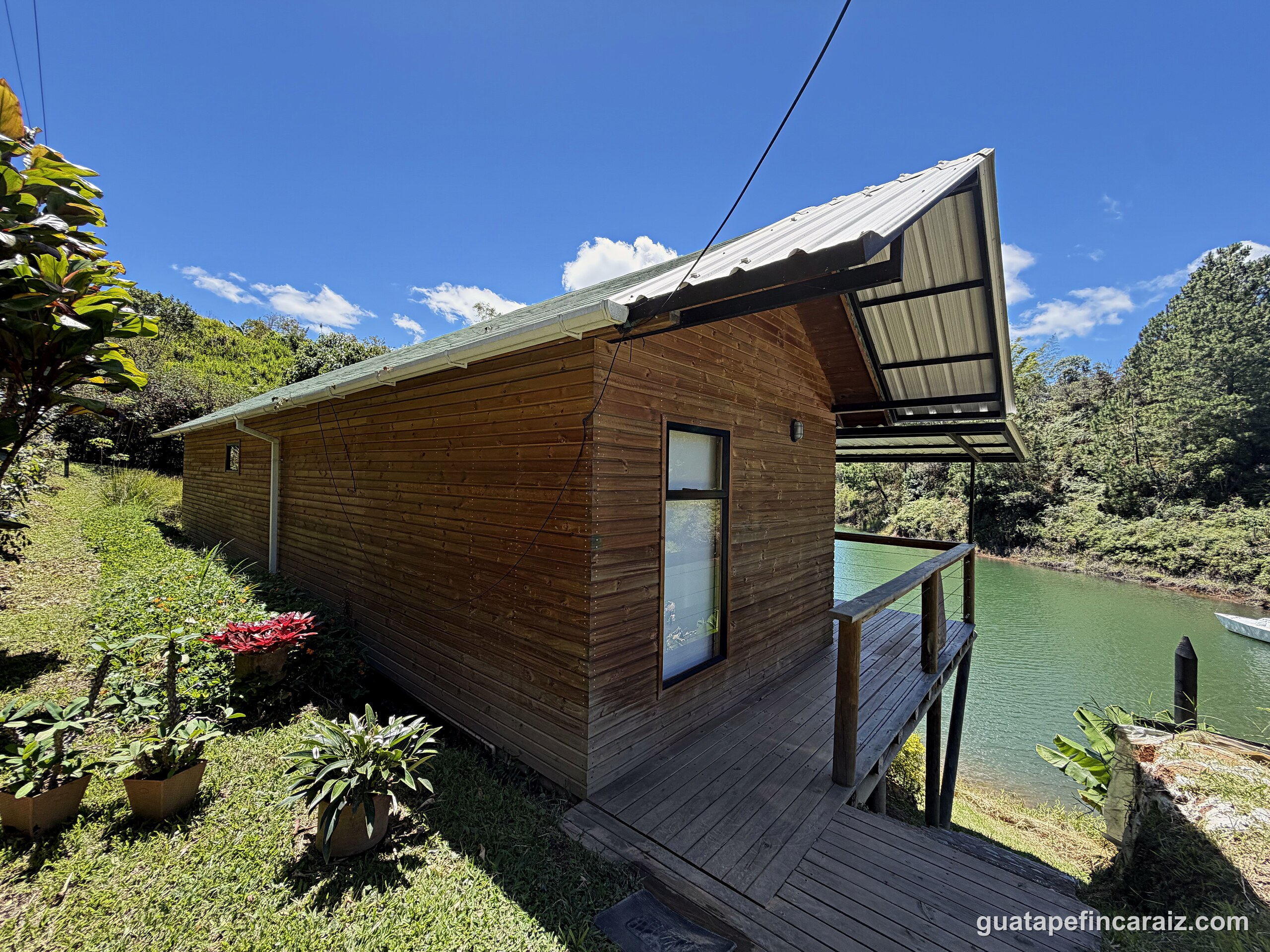 Cabaña del Embalse wood cabin exterior with covered deck extending toward the Guatapé-El Peñol reservoir