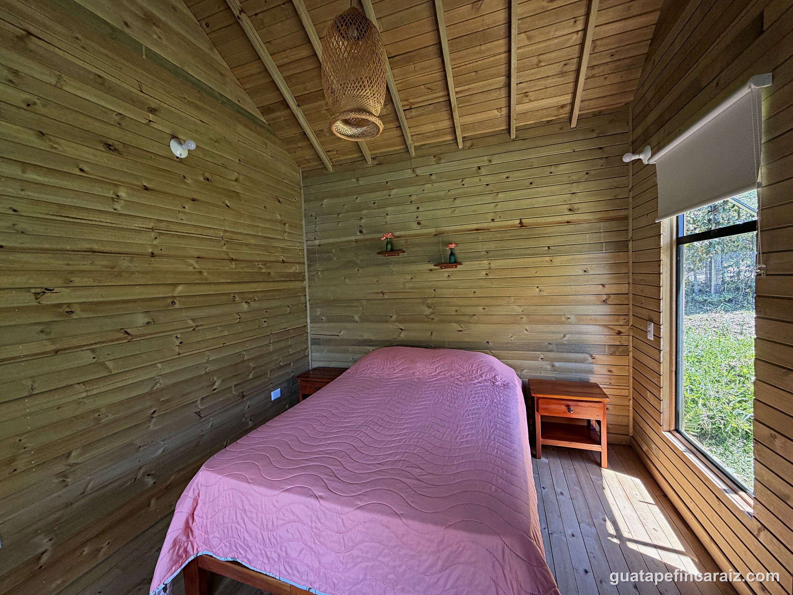 Primary bedroom at Cabaña del Embalse with wood plank walls and a window facing the garden