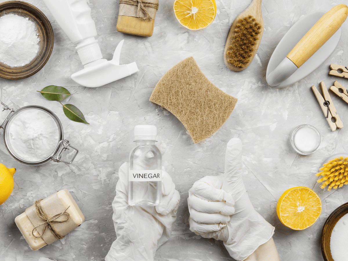 Close-up of eco-friendly cleaning products, including a vinegar and baking soda spray bottle, microfiber cloths, and a scrubbing brush on a clean bathroom counter.