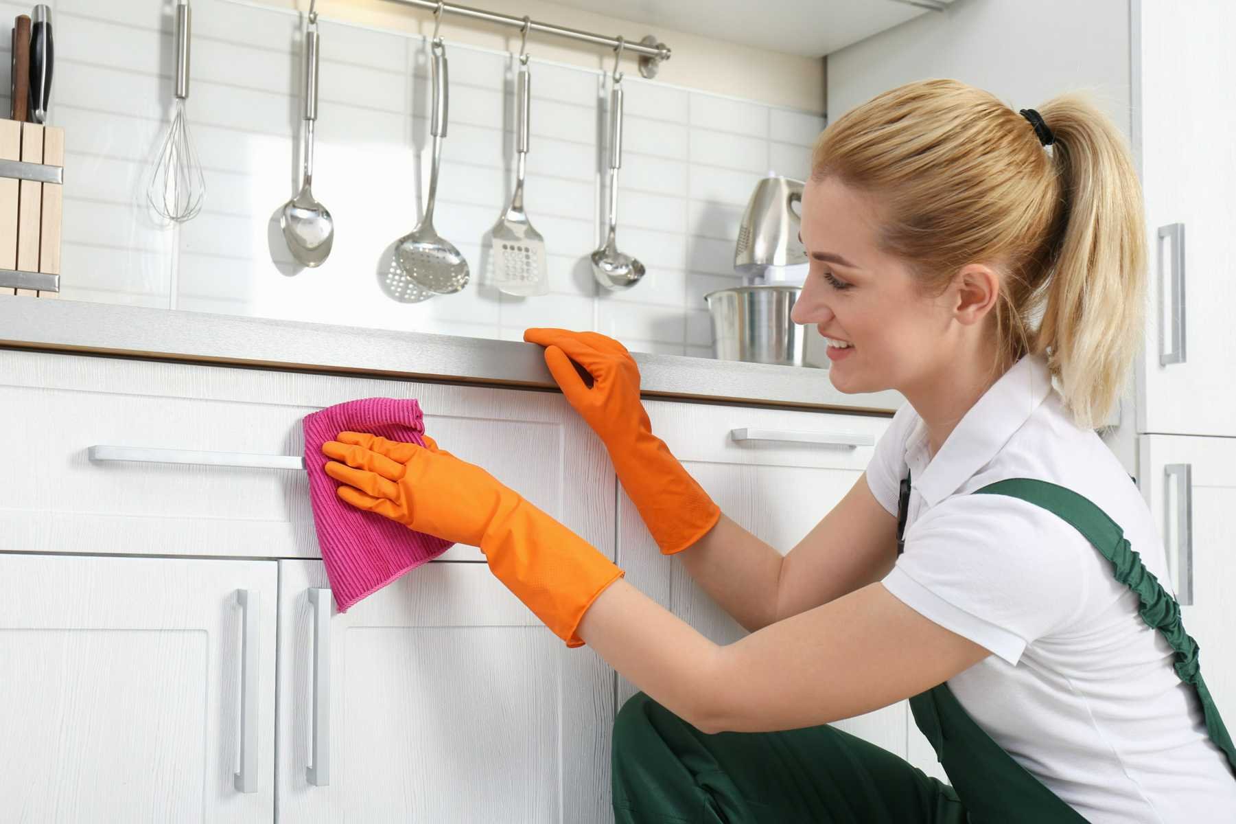 Close-up of a hand cleaning grease from kitchen cabinets using a microfiber cloth, demonstrating effective kitchen cleaning techniques.