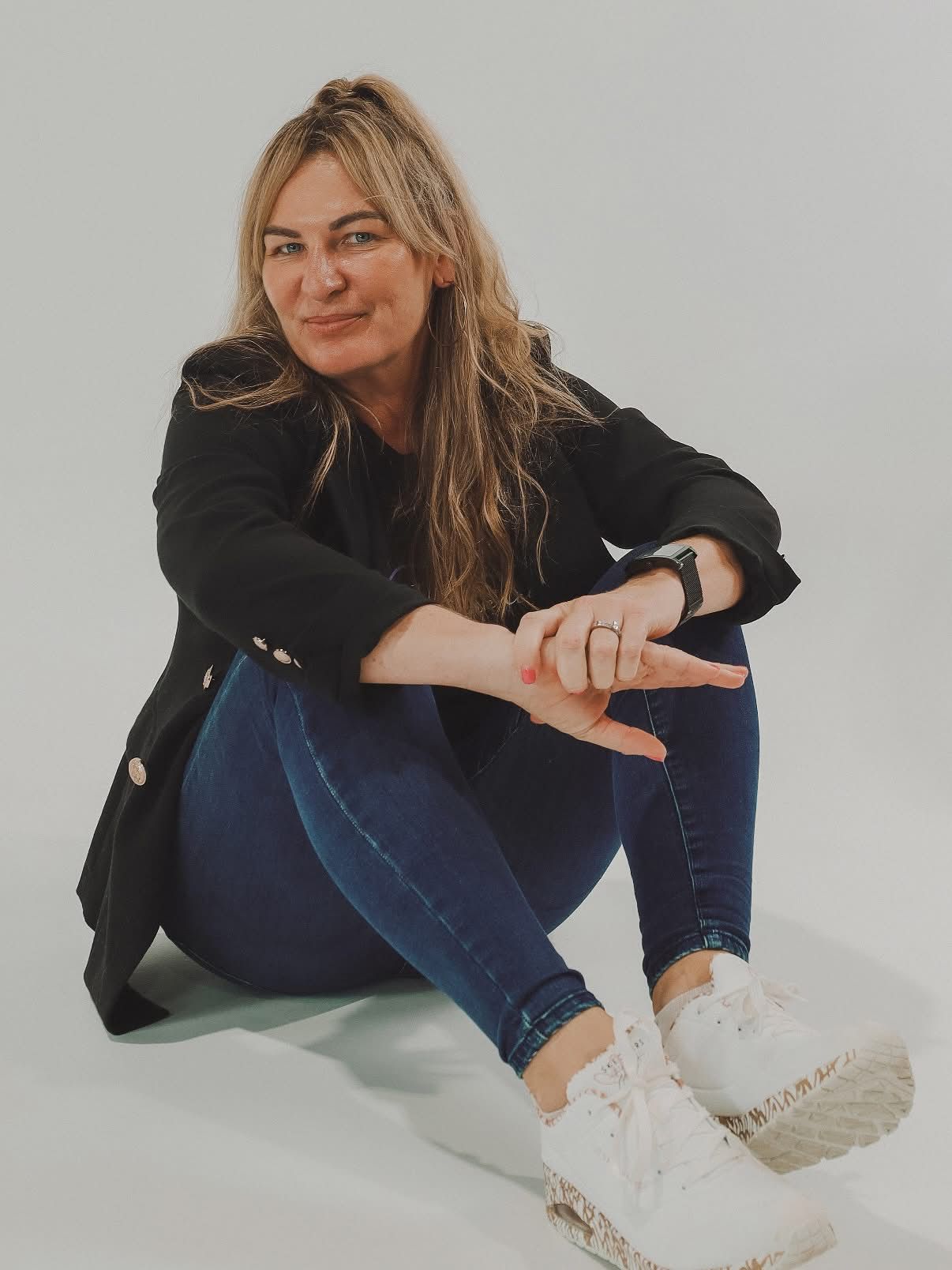 Katie Turner, founder of DVINE Experiences, sitting on a studio floor in a black jacket and jeans