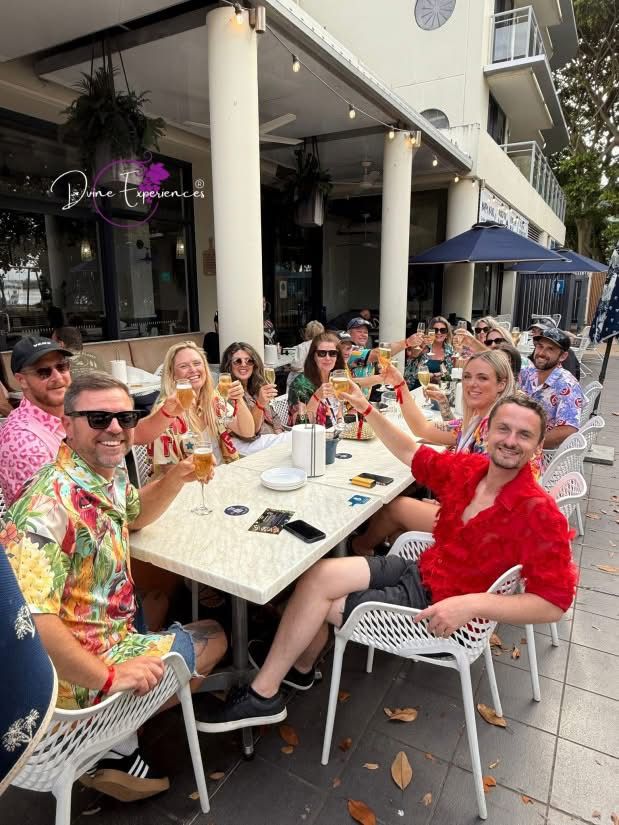 A mixed group raising their glasses at a long outdoor table on a restaurant terrace