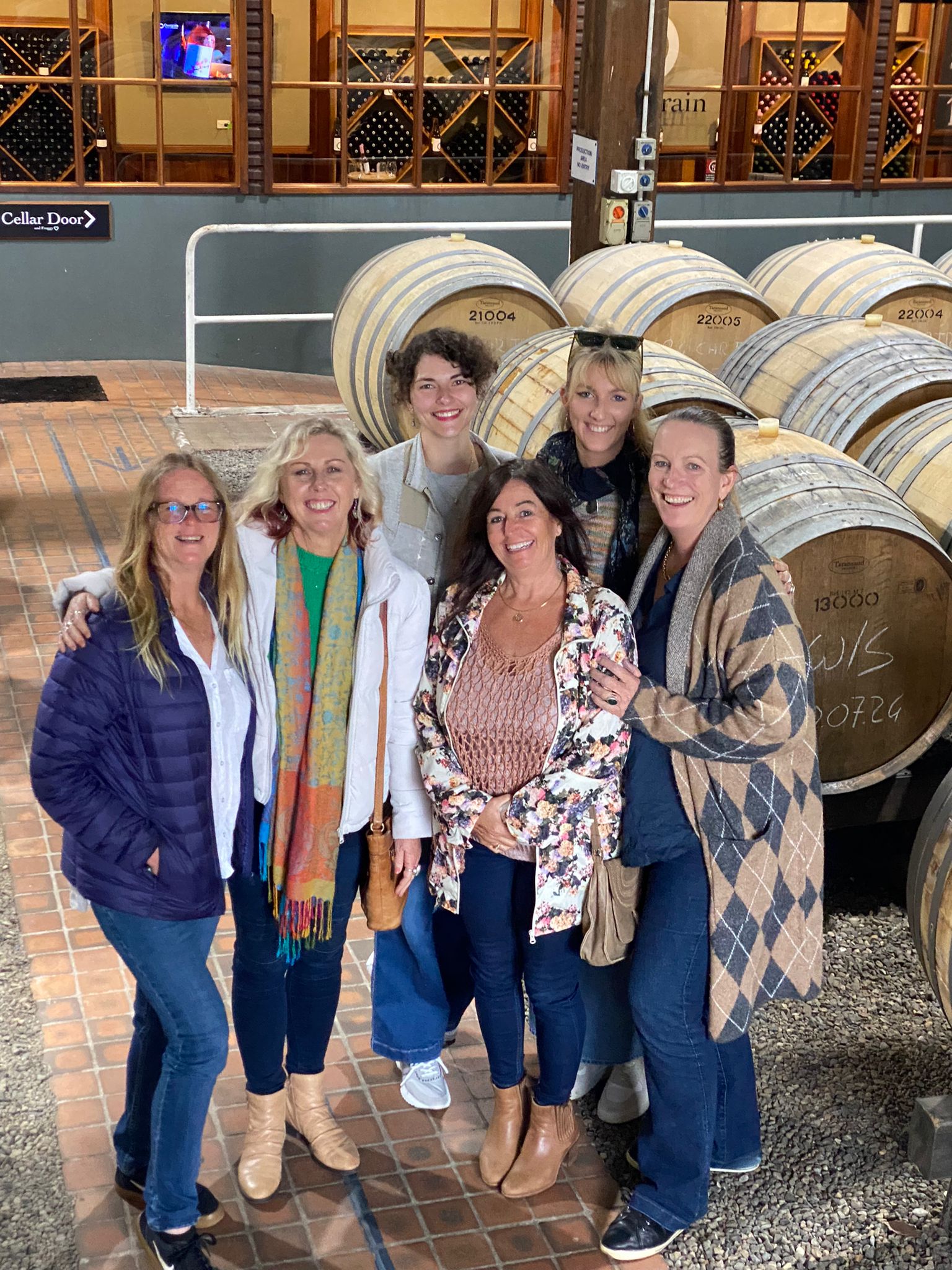 A group of women standing together in front of wine barrels at a cellar door