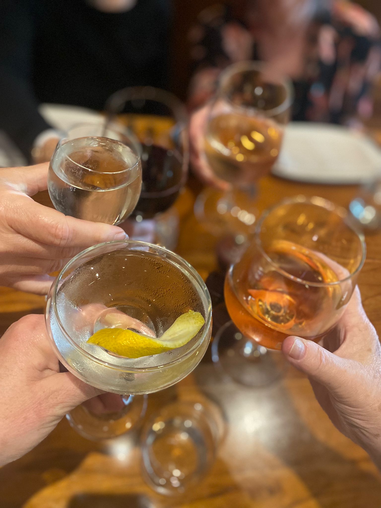 Glasses of beer and cocktails raised together in a toast over a timber table