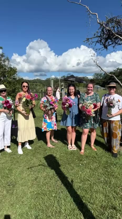 Pick & Sip guests standing in a row on the grass, each holding a bunch of freshly picked flowers