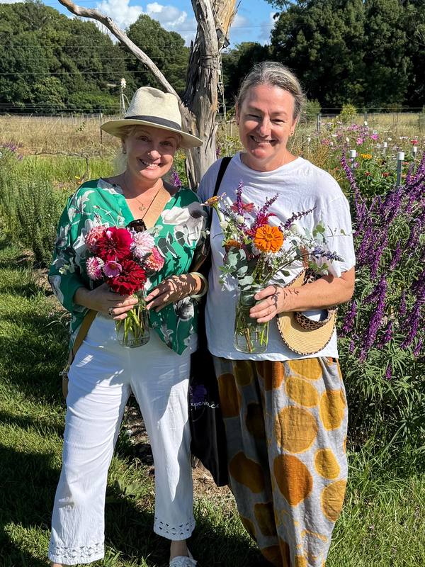 DVINE founder Katie Turner and a guest smiling in a flower field, each holding a jar of freshly picked flowers