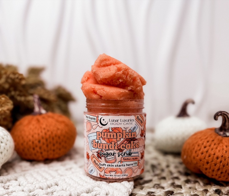 Lunar Luxuries Pumpkin Bundt Cake Sugar Scrub in its original jar, surrounded by knitted pumpkins.